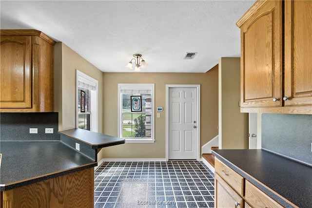 kitchen featuring kitchen peninsula, dark tile patterned flooring, a textured ceiling, and a notable chandelier