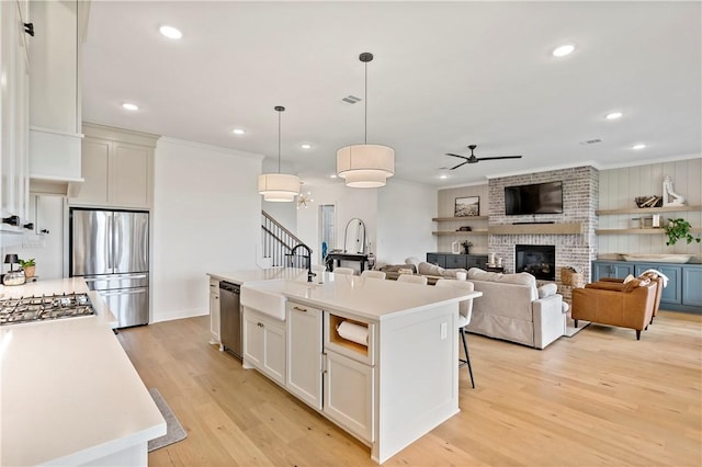 kitchen with a sink, appliances with stainless steel finishes, light countertops, light wood finished floors, and a ceiling fan