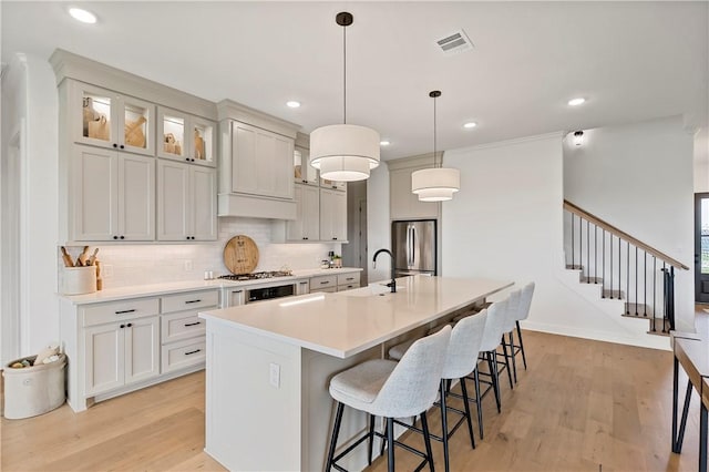 kitchen featuring a kitchen island with sink, stainless steel appliances, a breakfast bar, visible vents, and light wood-style flooring