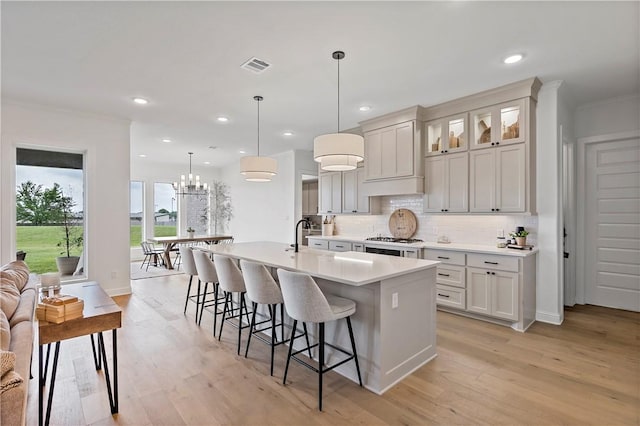 kitchen with stainless steel gas stovetop, a breakfast bar, light wood-type flooring, visible vents, and a center island with sink