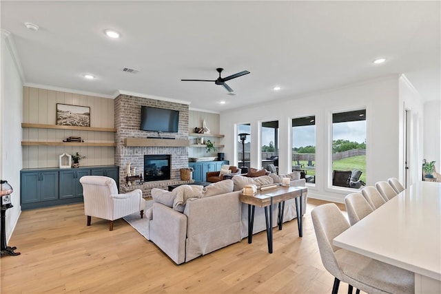 living area with crown molding, light wood-style flooring, visible vents, ceiling fan, and a brick fireplace