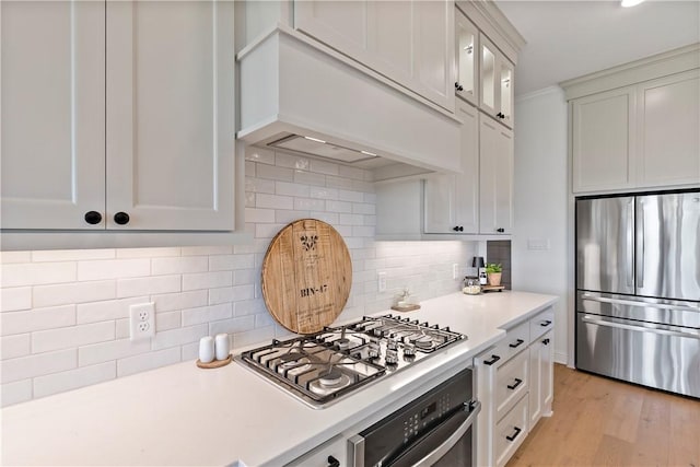kitchen featuring appliances with stainless steel finishes, light countertops, light wood-style flooring, and glass insert cabinets
