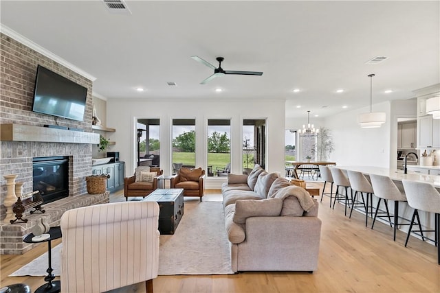 living room with a fireplace, visible vents, light wood-style flooring, and ceiling fan with notable chandelier