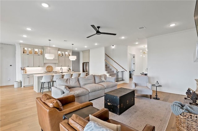 living area with recessed lighting, stairs, ceiling fan with notable chandelier, light wood finished floors, and baseboards
