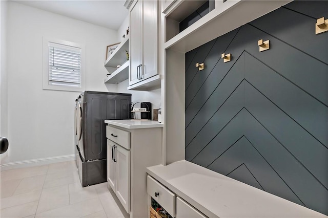 clothes washing area featuring baseboards, light tile patterned floors, separate washer and dryer, and cabinet space