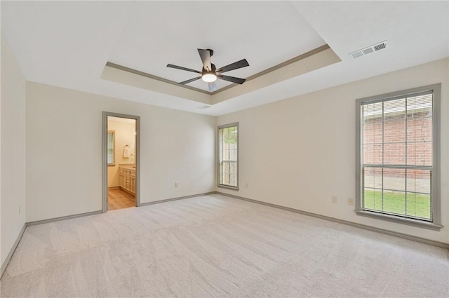 spare room with a tray ceiling, ceiling fan, and light carpet