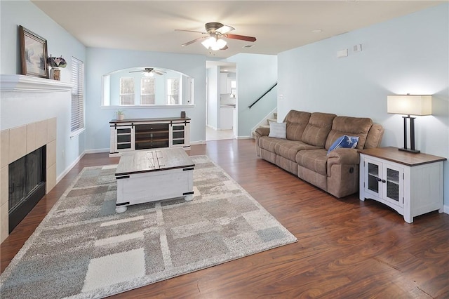 living room featuring a tile fireplace, dark hardwood / wood-style floors, and ceiling fan