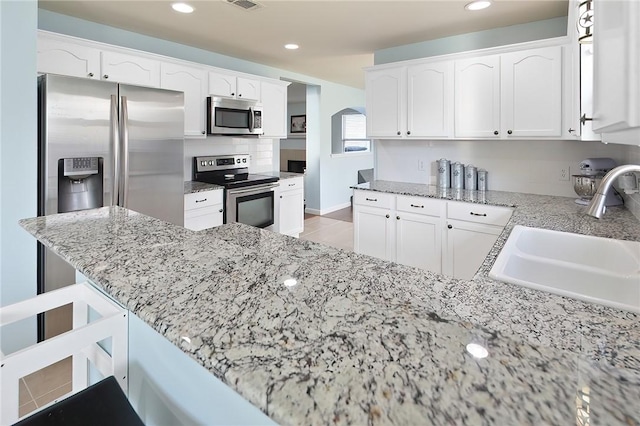 kitchen with white cabinetry, stainless steel appliances, light stone countertops, and sink