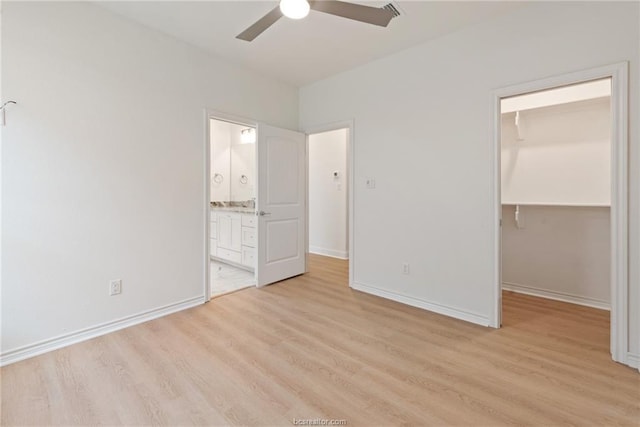 unfurnished bedroom featuring connected bathroom, a spacious closet, light wood-type flooring, a closet, and ceiling fan