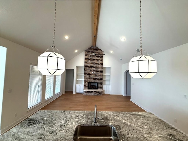 kitchen with sink, beam ceiling, wood-type flooring, a fireplace, and stone countertops