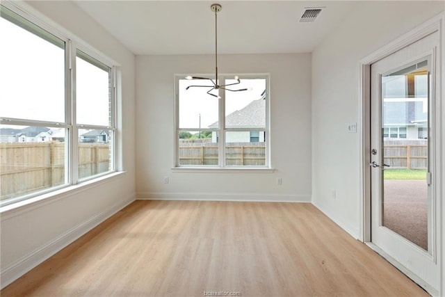 unfurnished dining area featuring a wealth of natural light, a notable chandelier, and light hardwood / wood-style flooring