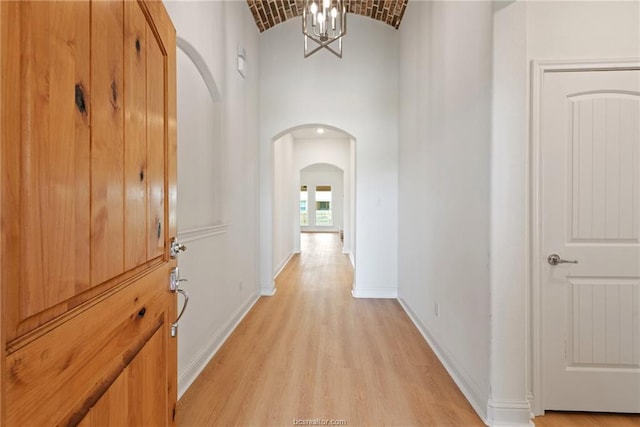 corridor with brick ceiling, vaulted ceiling, a chandelier, and light wood-type flooring