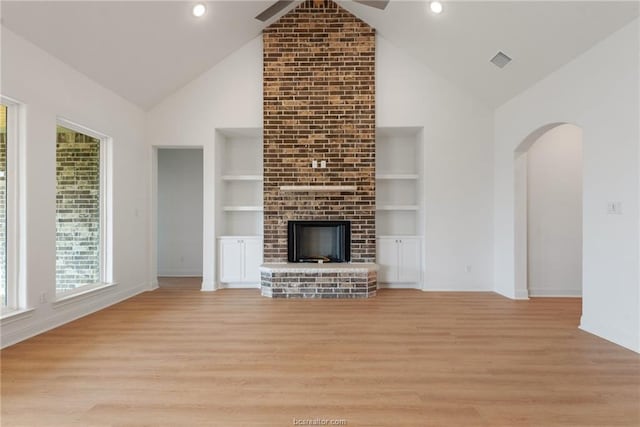 unfurnished living room with built in features, high vaulted ceiling, a brick fireplace, and light wood-type flooring