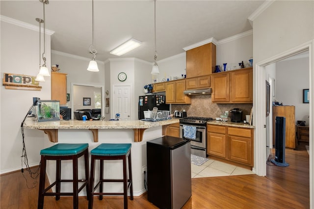 kitchen with stainless steel gas stove, black fridge, kitchen peninsula, pendant lighting, and light stone countertops