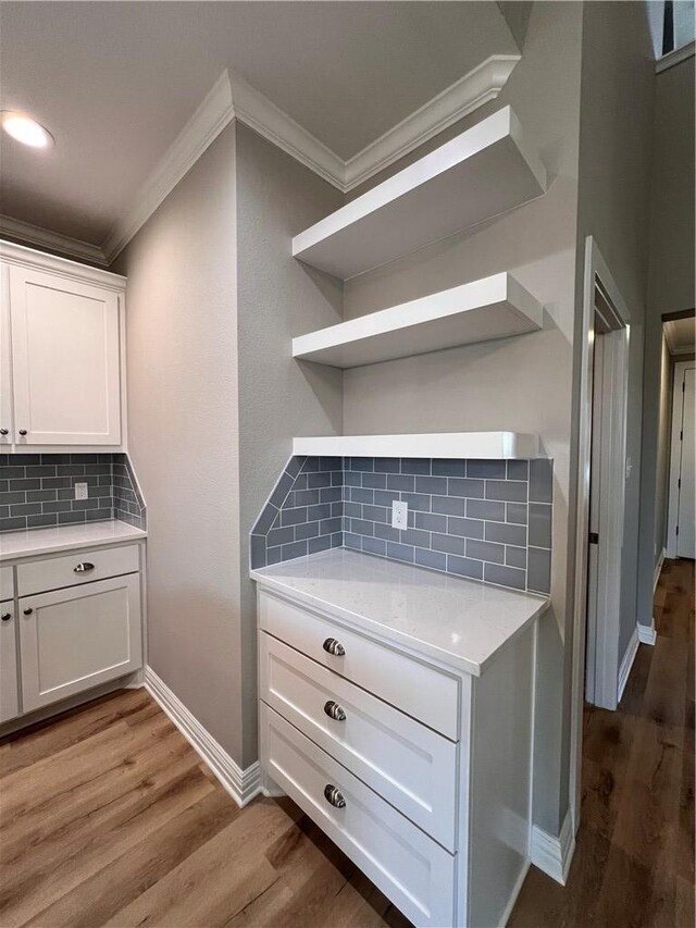 kitchen featuring decorative backsplash, hardwood / wood-style flooring, white cabinetry, and ornamental molding