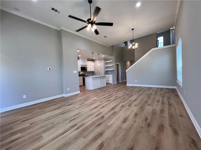 unfurnished living room with ceiling fan with notable chandelier, light hardwood / wood-style floors, crown molding, and sink