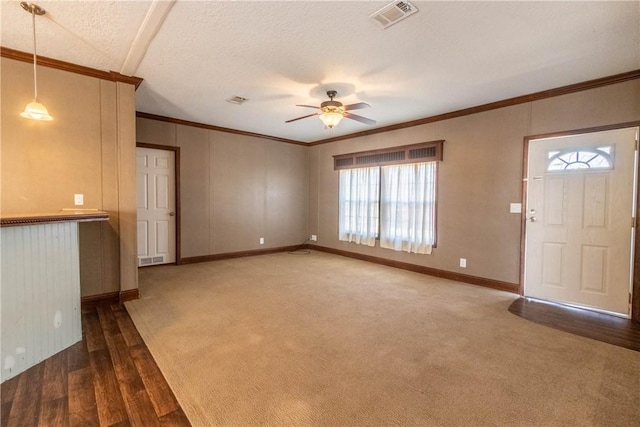 unfurnished living room featuring a textured ceiling, carpet floors, a ceiling fan, visible vents, and crown molding