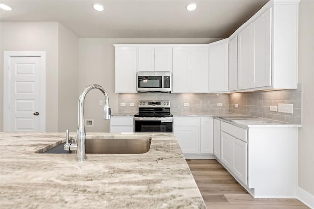 kitchen with sink, light stone counters, white cabinets, stainless steel appliances, and backsplash