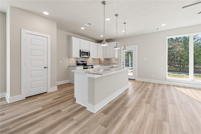 kitchen featuring pendant lighting, tasteful backsplash, white cabinetry, stainless steel appliances, and light stone countertops