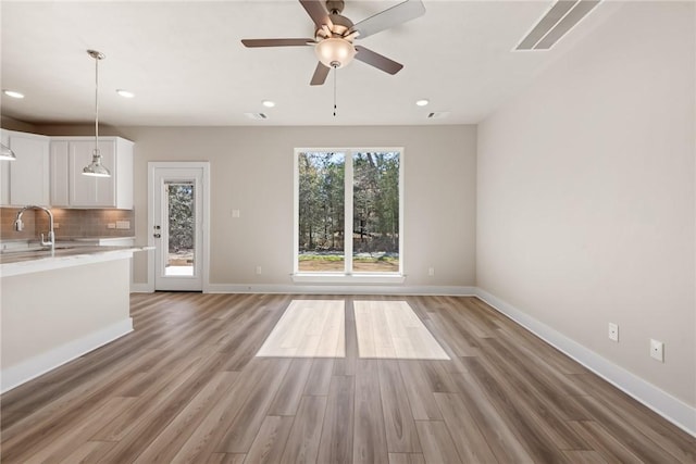 unfurnished living room with ceiling fan, sink, and light wood-type flooring