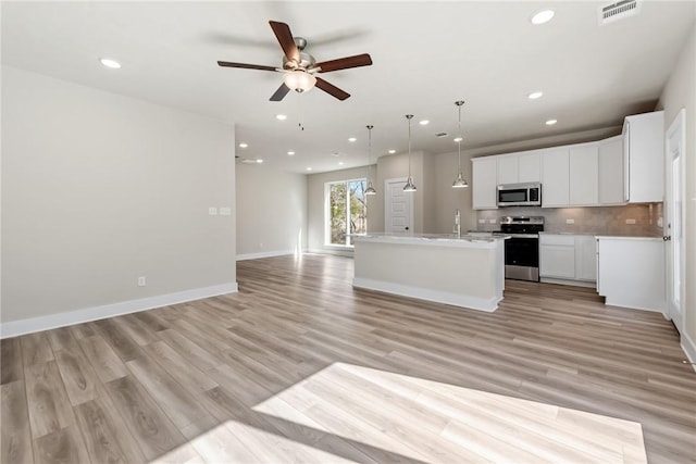 kitchen featuring light hardwood / wood-style flooring, appliances with stainless steel finishes, pendant lighting, a kitchen island with sink, and white cabinets