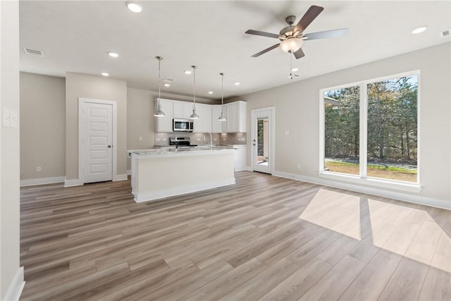 kitchen featuring appliances with stainless steel finishes, white cabinetry, decorative backsplash, hanging light fixtures, and light hardwood / wood-style floors