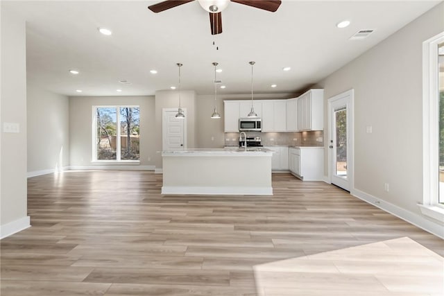 kitchen featuring white cabinetry, tasteful backsplash, decorative light fixtures, a center island with sink, and stainless steel appliances