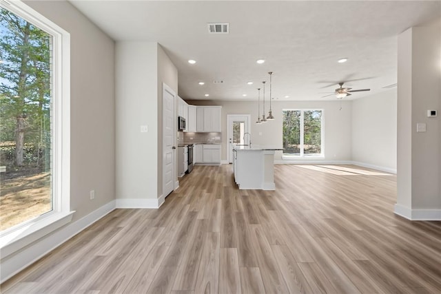 kitchen with pendant lighting, light hardwood / wood-style flooring, appliances with stainless steel finishes, white cabinets, and a center island with sink