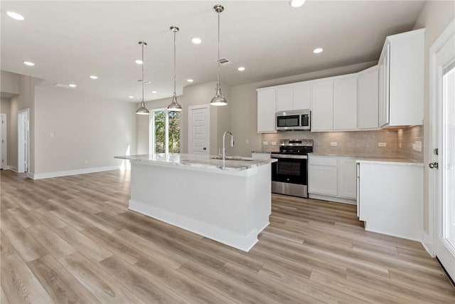 kitchen with sink, appliances with stainless steel finishes, hanging light fixtures, white cabinets, and a center island with sink