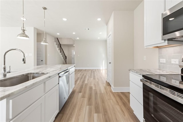 kitchen with sink, white cabinetry, light stone counters, decorative light fixtures, and stainless steel appliances