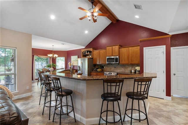 kitchen featuring a breakfast bar area, brown cabinets, stainless steel appliances, ceiling fan with notable chandelier, and backsplash