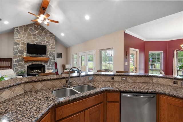 kitchen with dark stone counters, a sink, a stone fireplace, dishwasher, and open floor plan