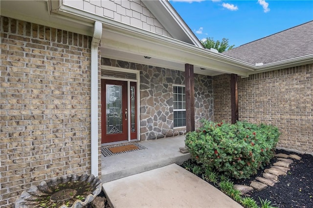 entrance to property with roof with shingles, brick siding, and stone siding