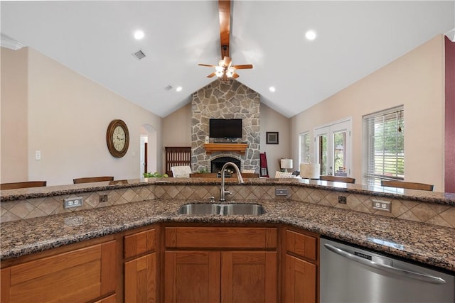 kitchen with dark stone counters, a sink, ceiling fan, dishwasher, and a stone fireplace