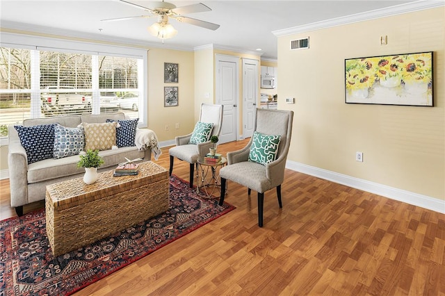 living area with visible vents, baseboards, ornamental molding, wood finished floors, and a ceiling fan