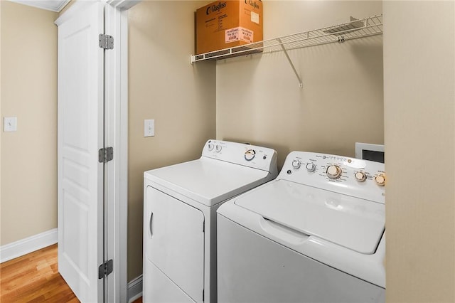 clothes washing area featuring laundry area, wood finished floors, baseboards, and washing machine and clothes dryer