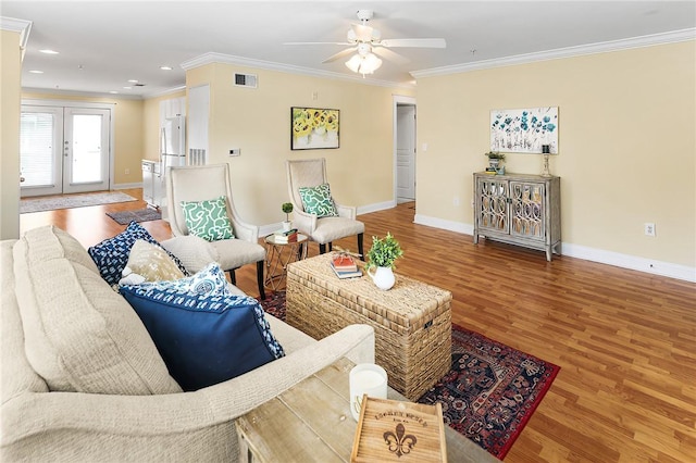 living area featuring visible vents, crown molding, baseboards, wood finished floors, and a ceiling fan