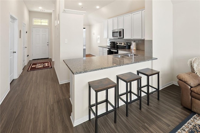 kitchen with white cabinets, a kitchen breakfast bar, kitchen peninsula, stone countertops, and appliances with stainless steel finishes