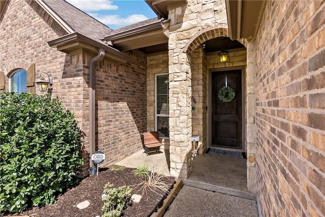 view of exterior entry with stone siding, brick siding, and a shingled roof