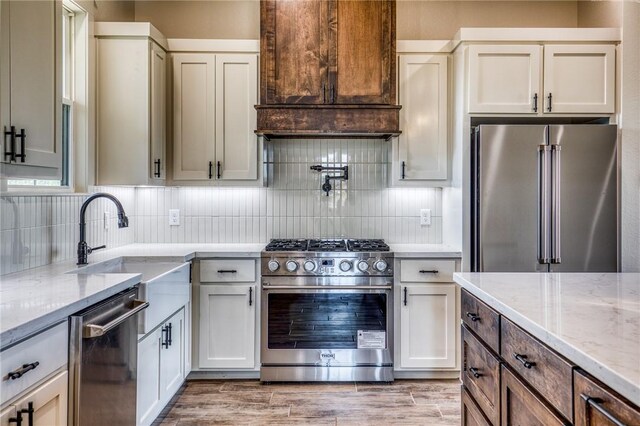 kitchen with tasteful backsplash, wood-type flooring, sink, stainless steel appliances, and light stone countertops