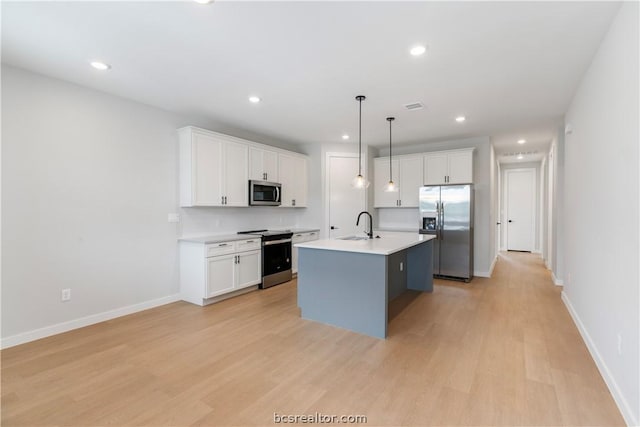 kitchen with white cabinets, appliances with stainless steel finishes, a center island with sink, and decorative light fixtures