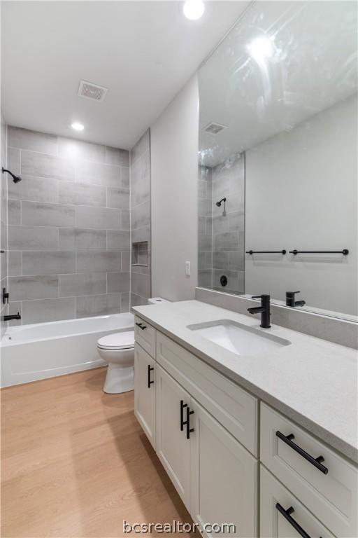 full bathroom with tiled shower / bath, vanity, wood-type flooring, and toilet