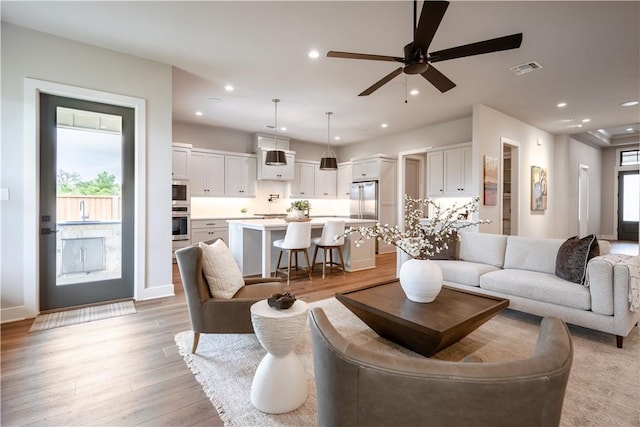 living room featuring ceiling fan, sink, and light wood-type flooring