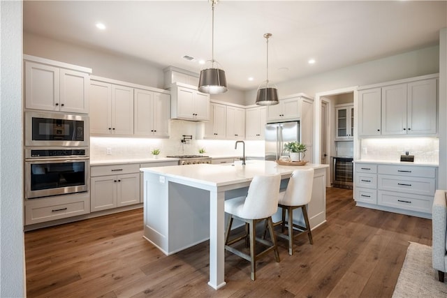 kitchen with pendant lighting, a breakfast bar, white cabinetry, built in appliances, and an island with sink