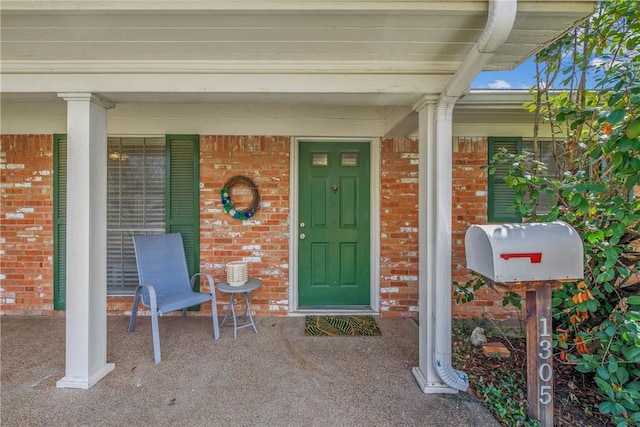 doorway to property featuring a porch and brick siding