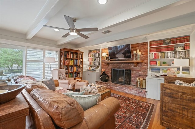 living area with wood finished floors, beamed ceiling, a fireplace, visible vents, and a ceiling fan