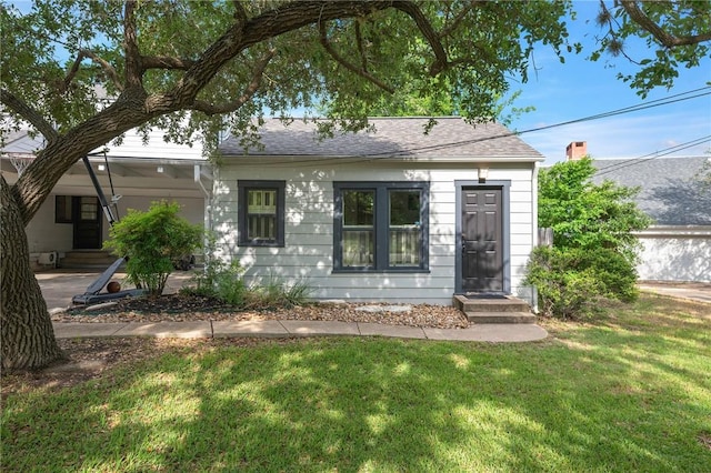 view of front facade with a front lawn, a shingled roof, and entry steps