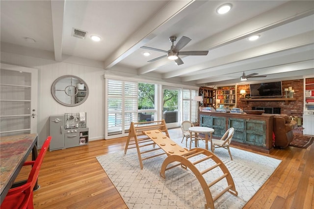 dining room featuring light wood finished floors, beam ceiling, a fireplace, a ceiling fan, and visible vents