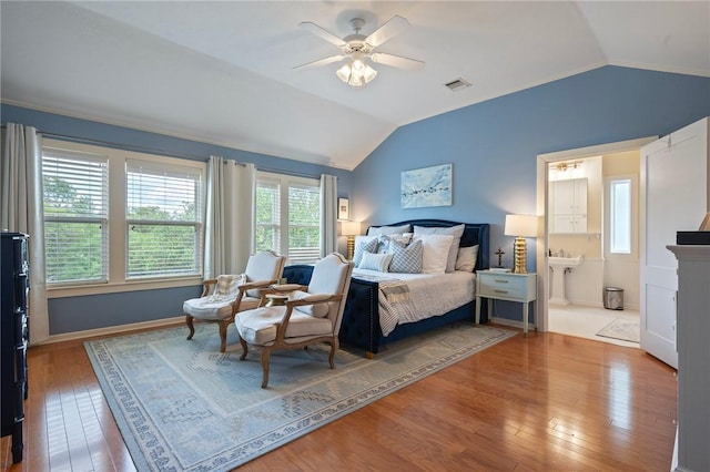 bedroom featuring lofted ceiling, ensuite bath, a ceiling fan, visible vents, and wood finished floors