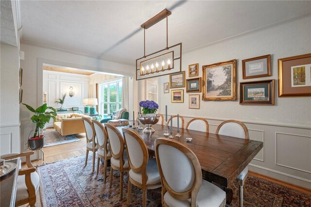 dining area featuring ornamental molding, an inviting chandelier, wood finished floors, and a decorative wall